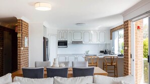 A modern kitchen with white cabinets, a microwave, and a dining area with a table and chairs. - Bella Vista 1 - 3 bedroom Apartment Ocean View (Mollymook)