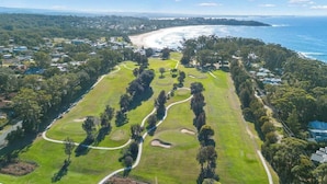 An aerial view of a golf course with a coastal backdrop, surrounded by residential areas. - Bella Vista 1 - 3 bedroom Apartment Ocean View (Mollymook)