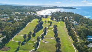 An aerial view of a golf course with a coastal backdrop, surrounded by residential areas. - Bella Vista 1 - 2 Bedroom Apartment Ocean Views (Mollymook)