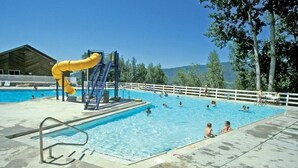 A swimming pool with a yellow slide, a diving board, and a fenced area.