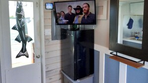 Ett rum med en tv som är monterad på väggen, en dörr med en fiskdekor, ett kylskåp och en liten hylla.