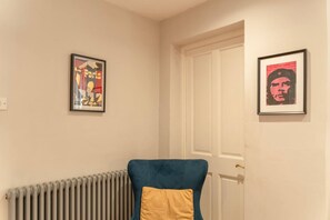 Una habitación con un radiador, una silla azul con un cojín amarillo y dos carteles enmarcados en la pared.