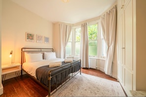 A bedroom with a bed, bedside table, and a window with curtains. - Roomy 2 Bed Garden Flat Quick Links to Central (London)