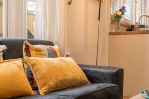 Ein schwarzes Ledersofa mit gelben Kissen, ein Fenster mit Jalousien und eine Vase mit Blumen auf der Fensterbank.