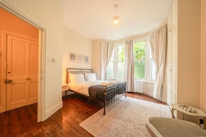 A bedroom with a bed, a bedside table, a window with curtains, and a door. - Roomy 2 Bed Garden Flat Quick Links to Central (London)