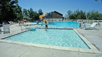 A swimming pool with a slide, lounge chairs, and a covered area.