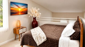 A bedroom with a bed, a nightstand, a vase with white flowers, a painting of a sunset, and a window with blinds. - Luxurious & Cozy Loft ~ 5 Stars Location - King Bed - Private Patio Retreat (Los Angeles)