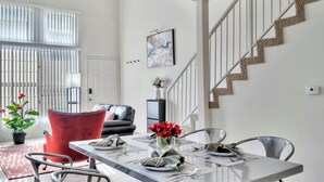 A dining area with a table set for four, a red chair, a staircase, and a door in the background. - Luxurious & Cozy Loft ~ 5 Stars Location - King Bed - Private Patio Retreat (Los Angeles)