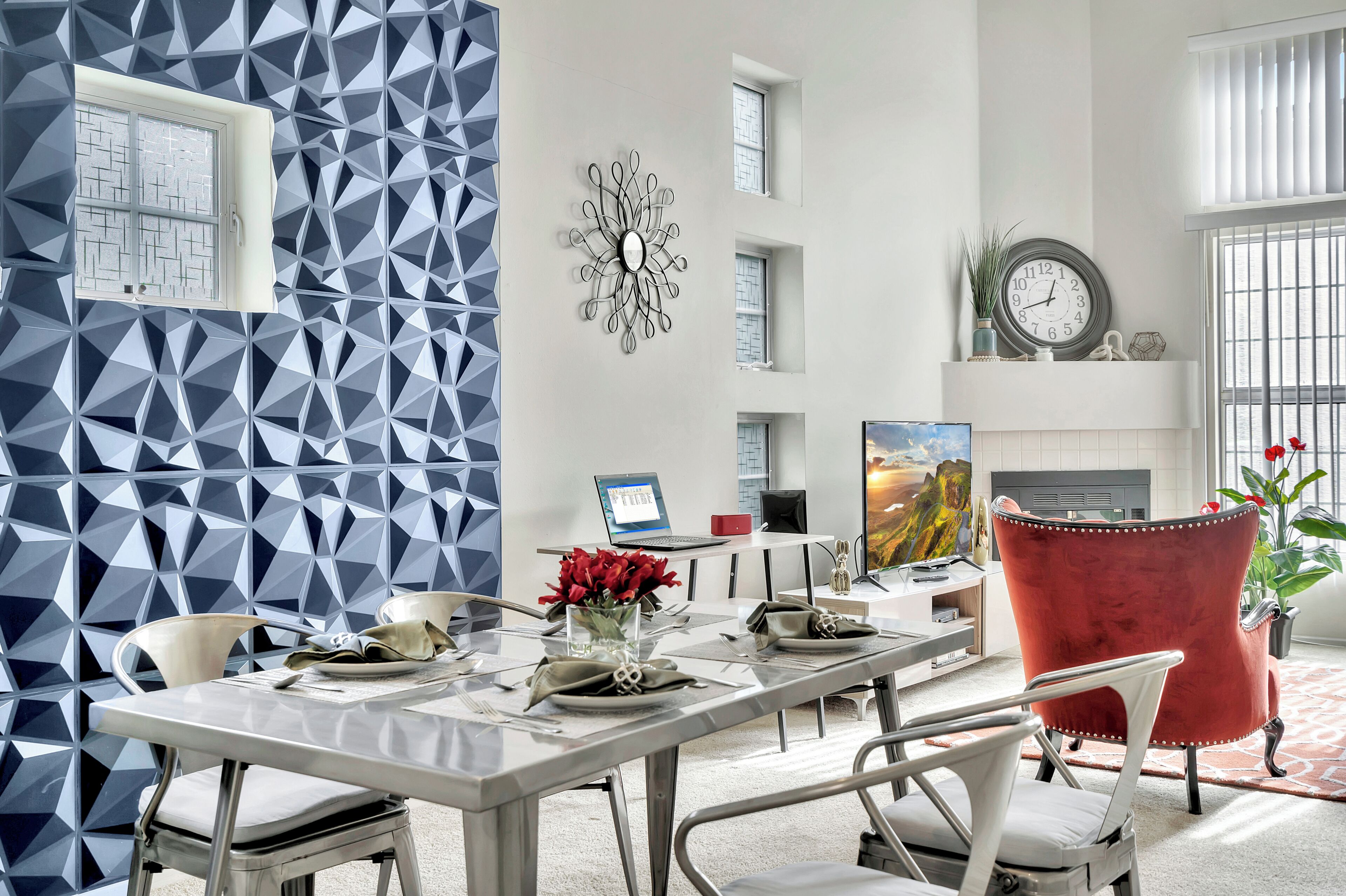 Een moderne eethoek met een wand met een geometrisch patroon, een decoratieve klok en een rode stoel.