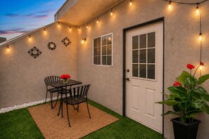 Eine Terrasse mit Tisch, Stühlen, einer Tür, Lichterketten und einem Blumentopf.