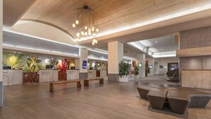 Eine großzügige Lobby mit Holzboden, einem Empfangstresen, Sitzbereichen und einer modernen Chandelier.