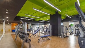 Ein Fitnessraum mit Trainingsgeräten, Holzboden und grünen Deckenleuchten.