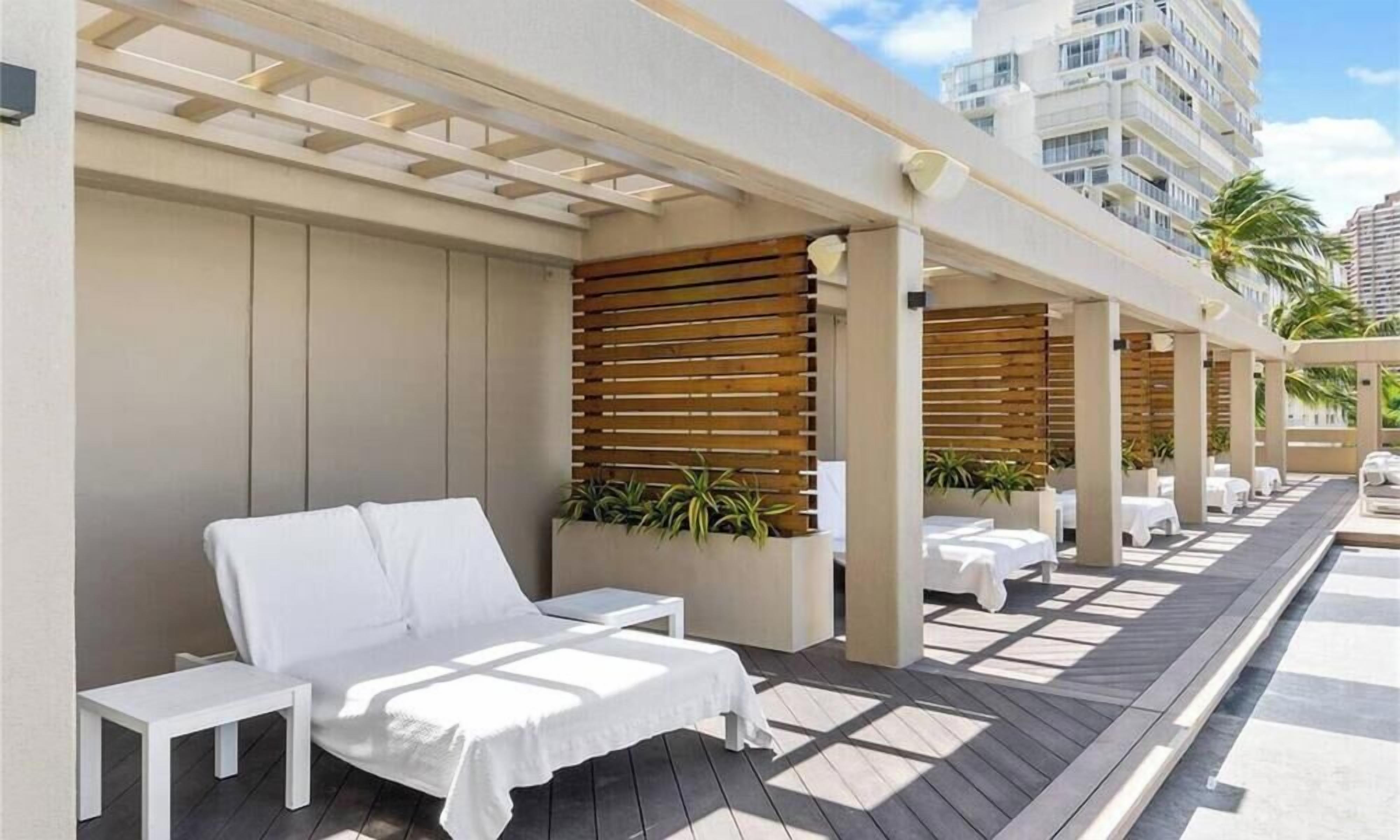 A rooftop lounge area with a white sofa, small tables, and potted plants.