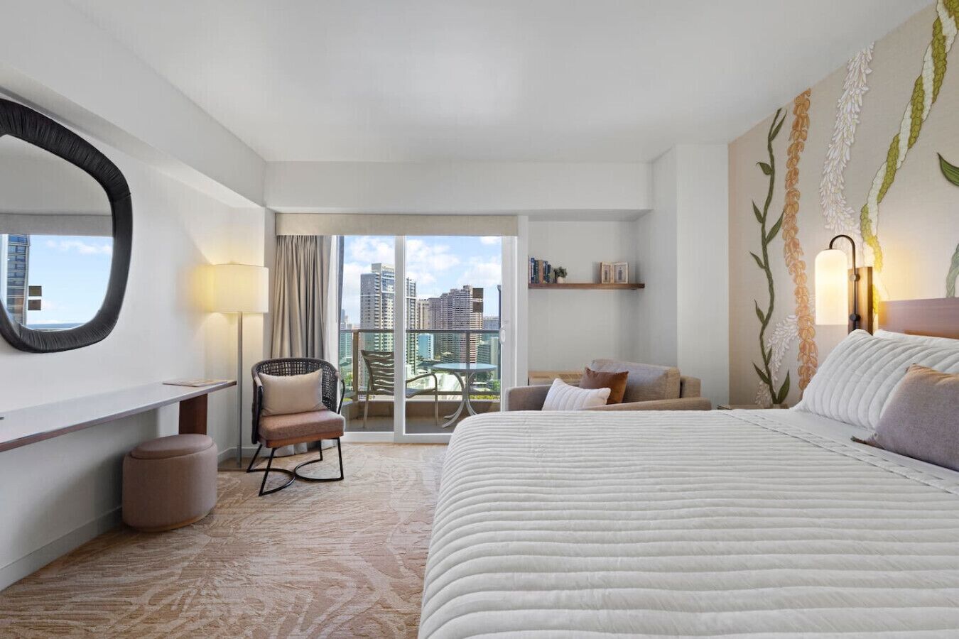 Una camera d'albergo con un letto, una sedia, una scrivania, un'ampia finestra con vista sulla città e un balcone.