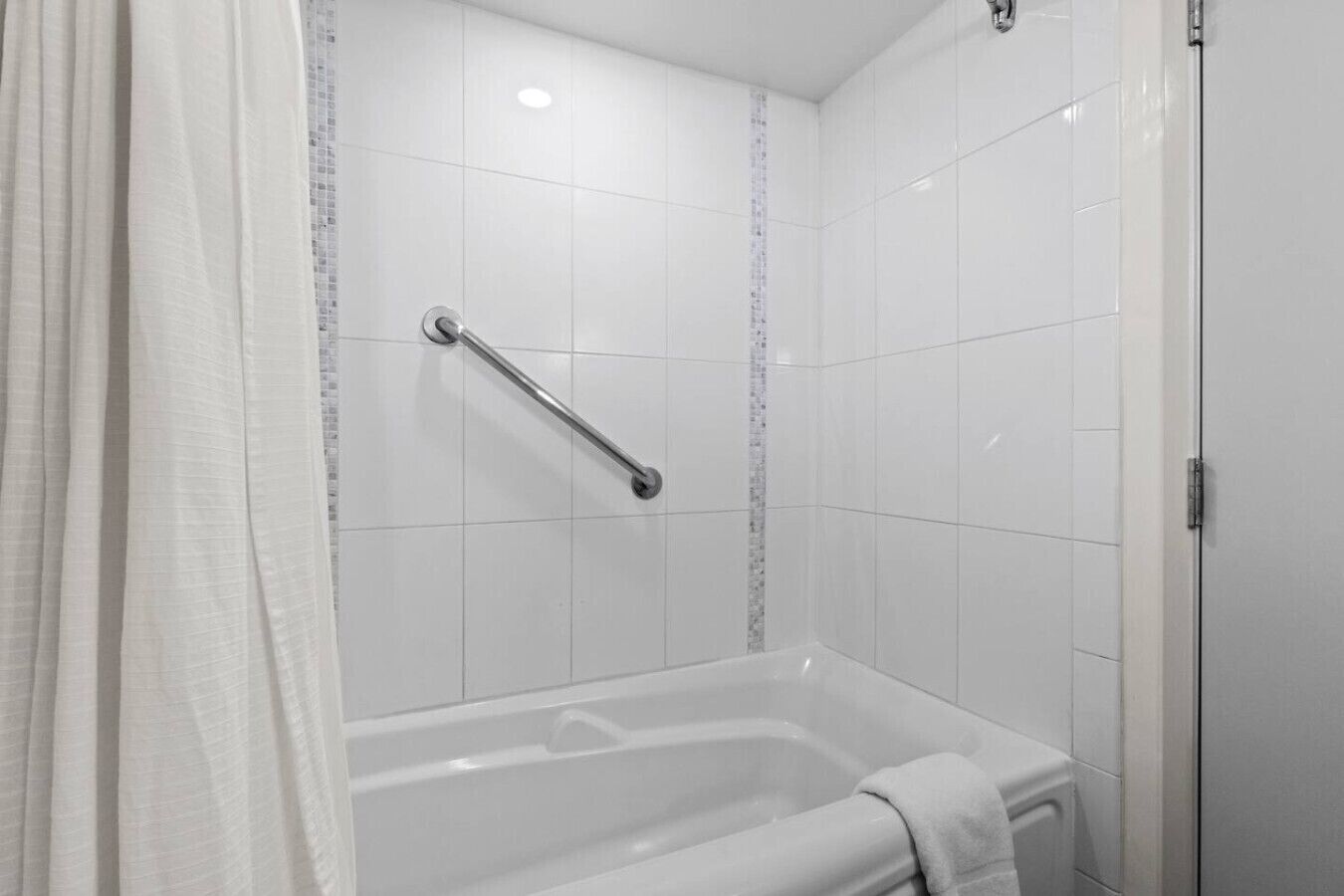 A bathroom with white tiled walls, a bathtub, a shower with a grab bar, and a door.