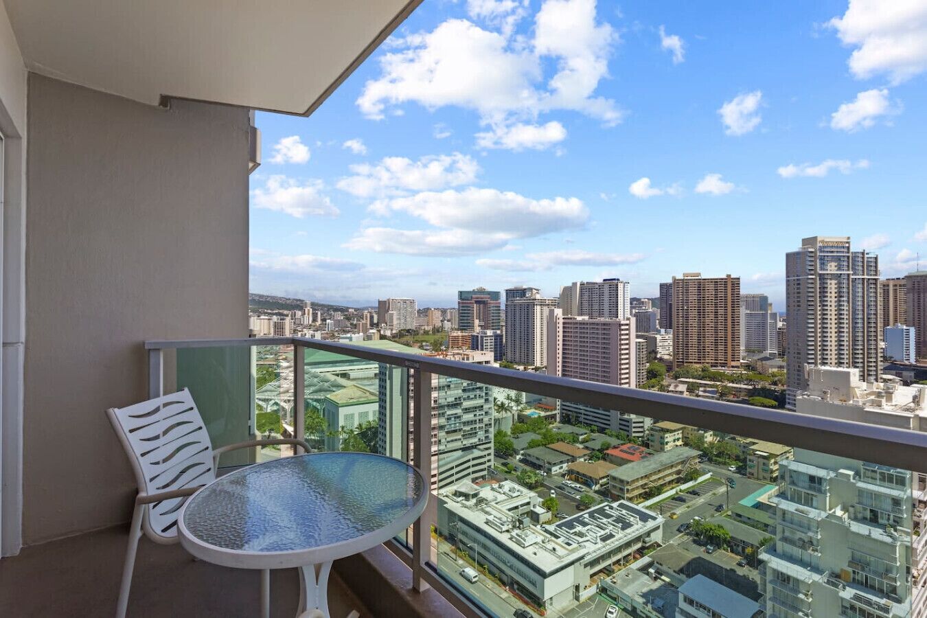 A balcony with a table and chair, overlooking a cityscape with high-rise buildings.