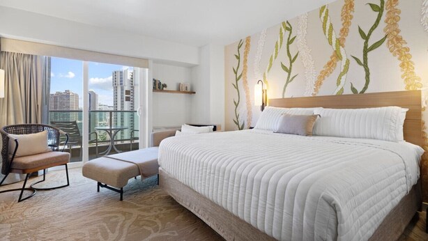 Ein Hotelzimmer mit einem großen Bett, einem Sessel, einem kleinen Tisch und Blick auf die Stadt.