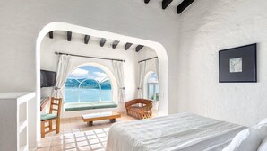 Un dormitorio con cama, una silla, un banco y vista al mar.