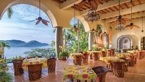 A restaurant with outdoor seating, tables with floral tablecloths, and a view of the sea. - Zihuatanejo | Compact Ocean Retreat | Pool + Beach (Zihuatanejo)