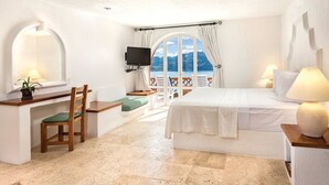 A bedroom with a bed, a desk with a chair, a TV, and a view of the sea. - Zihuatanejo | Compact Ocean Retreat | Pool + Beach (Zihuatanejo)