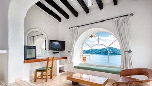 A room with a TV, a wooden chair, a bench, and a view of the sea. - Zihuatanejo | Compact Ocean Retreat | Pool + Beach (Zihuatanejo)