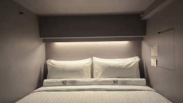 A single bed with a headboard, two pillows, and a bedside table with a lamp.