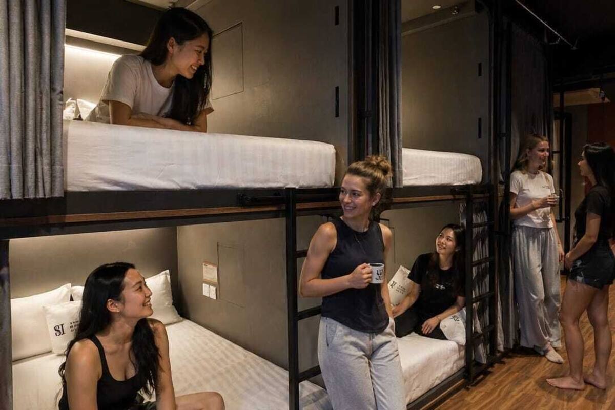 Une chambre de type dortoir, avec des lits superposés, un plancher en bois et une grande fenêtre.
