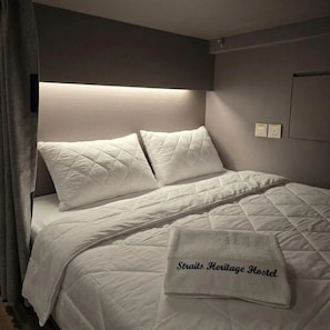 Un lit bien fait, avec une couette blanche matelassée, deux oreillers et une serviette pliée ornée d’un motif.