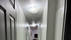 Un pasillo estrecho con suelo de madera, paredes blancas y un ventilador de techo.
