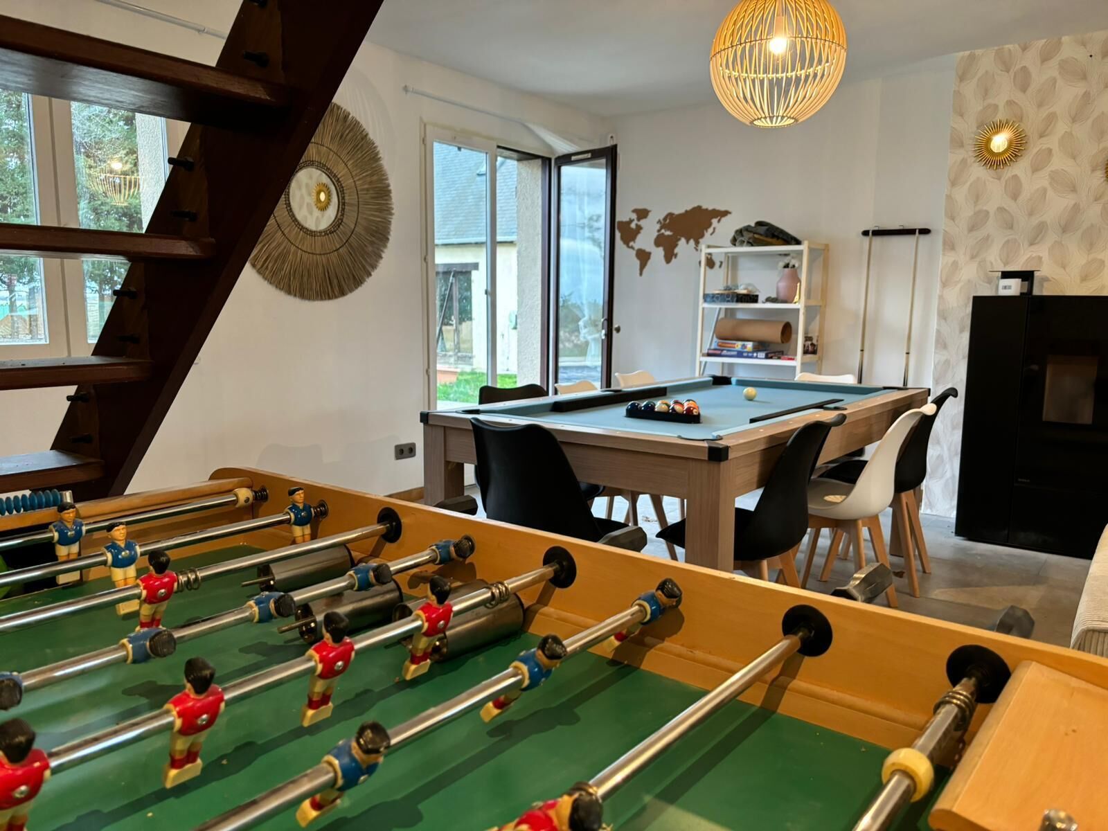 A room with a foosball table, billiards table, and a world map on the wall.