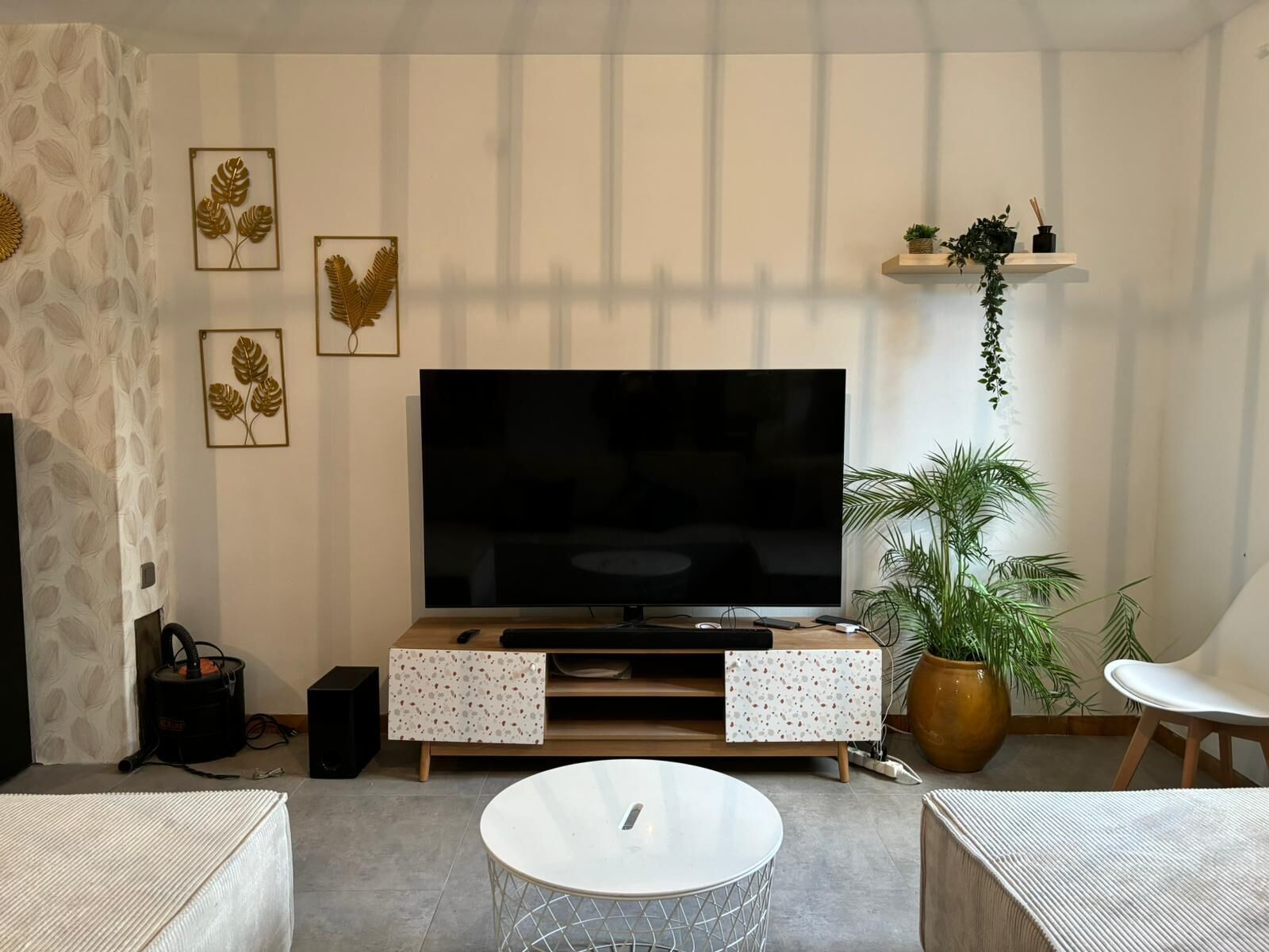 Un salon comprenant un téléviseur, deux tables d’appoint, une table basse, un canapé, un haut-parleur et des œuvres d’art décoratives accrochées au mur.