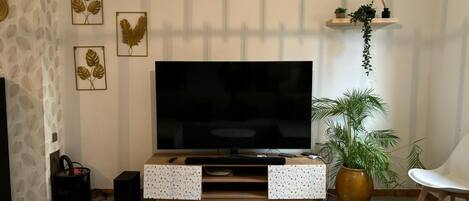 Un salon comprenant un téléviseur, deux tables d’appoint, une table basse, un canapé, un haut-parleur et des œuvres d’art décoratives accrochées au mur.