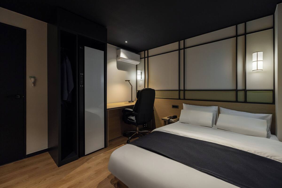 Quarto de hotel com cama, escrivaninha, cadeira e guarda-roupa.