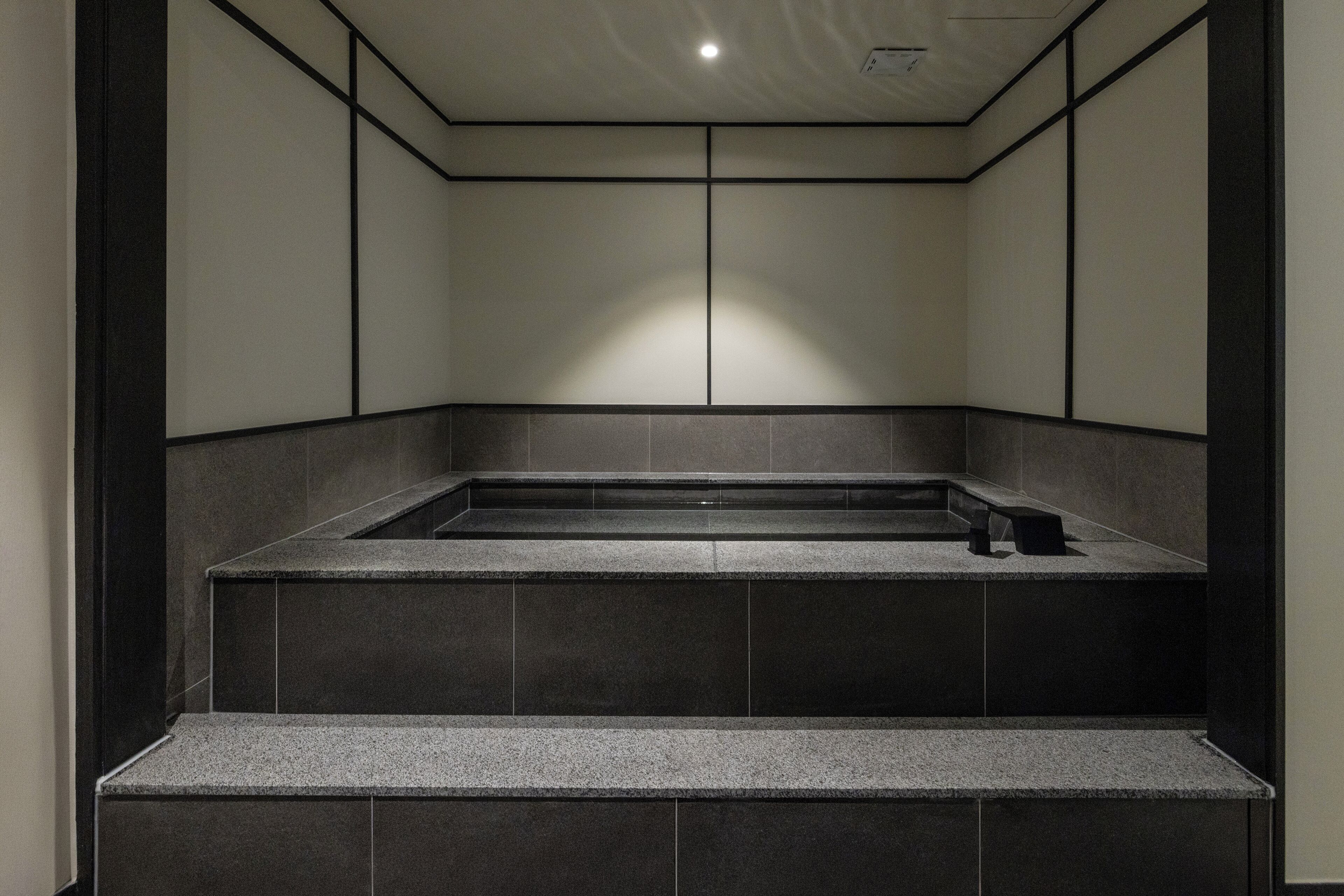 A modern bathroom with a freestanding bathtub, dark tiled walls, and a recessed ceiling light.