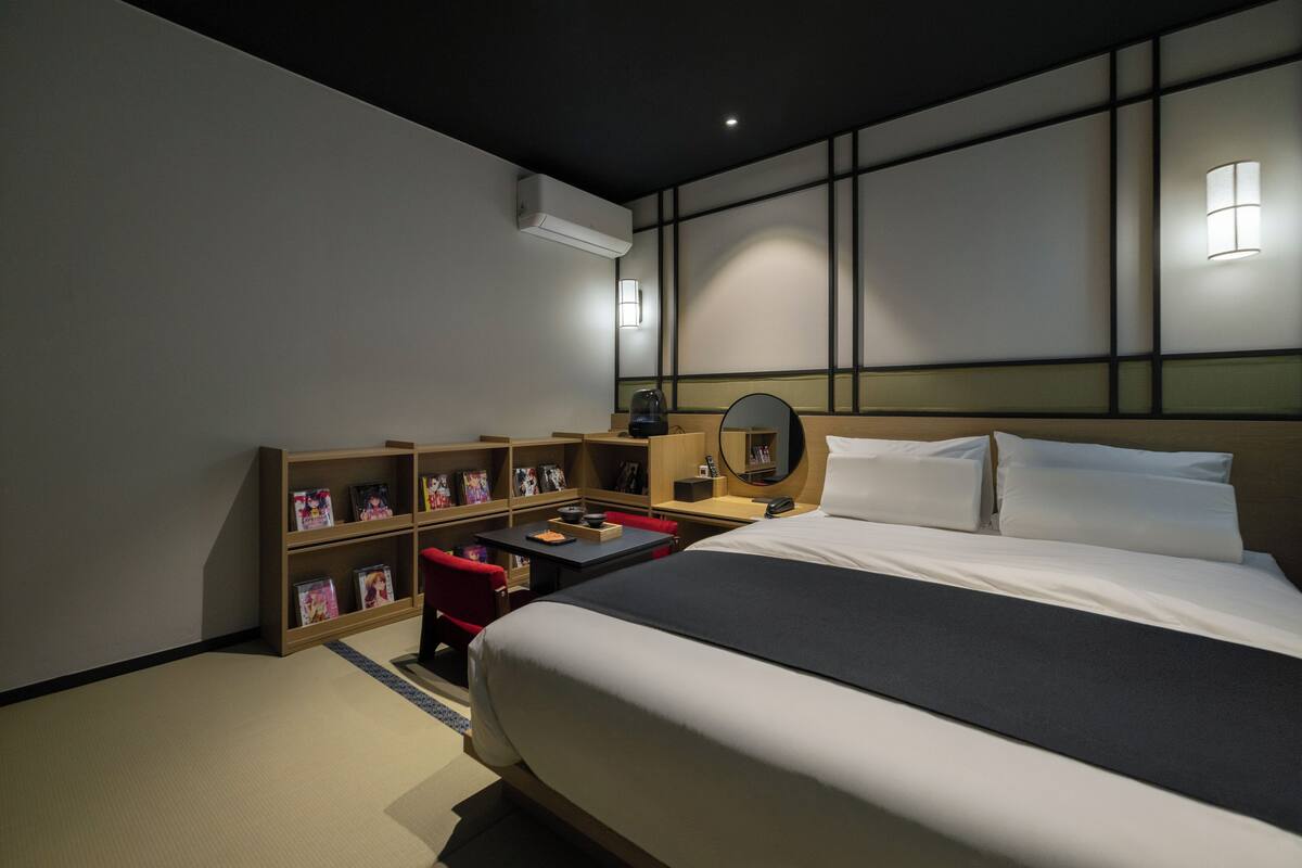 Quarto de hotel com uma cama grande, uma escrivaninha com cadeira, estante e espelho fixado na parede.