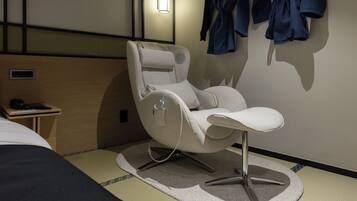 A modern hotel room with a massage chair, a bedside table with a phone, and a wall-mounted robe rack.