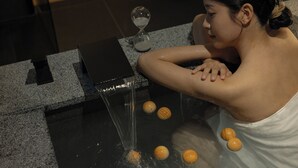A person relaxing in a spa setting with a water feature and an hourglass.