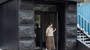 A person standing at a modern building entrance with stone accents and a blue staircase.