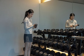 A person standing in a room with a large mirror reflecting their image, surrounded by multiple rows of black dumbbells on a rack. - Mitasuya Ryokan Hotel by Anook Gwangju (Gwangju)