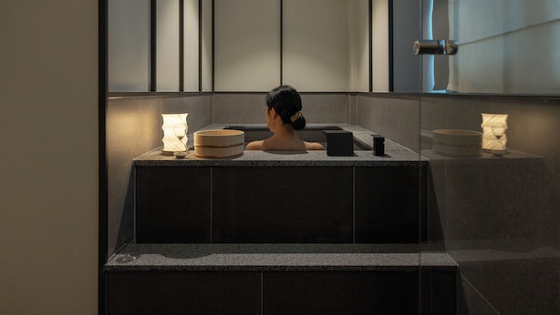 A spa area with a person in a hot tub, a towel, and a small table with a candle.