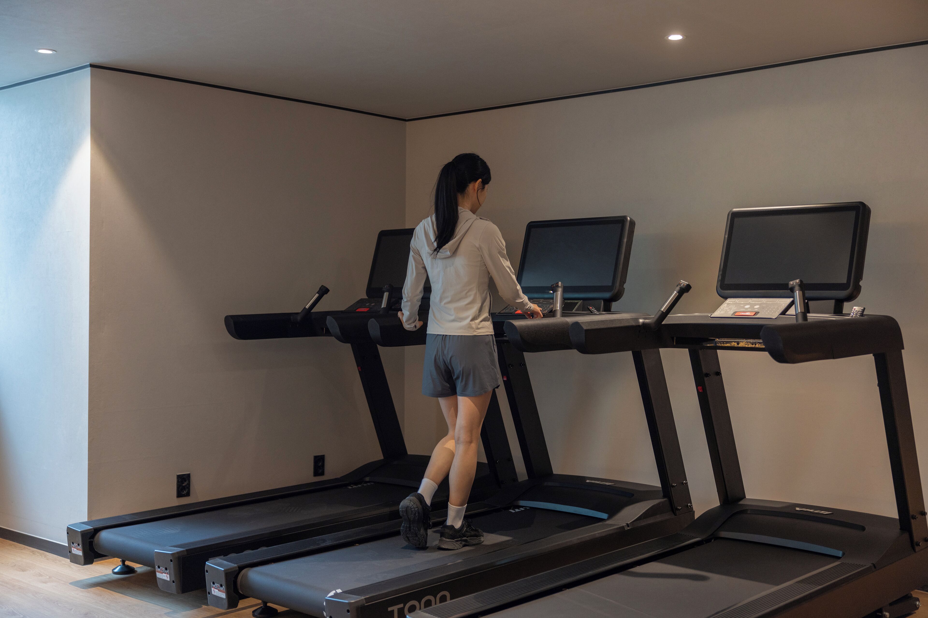 A woman walking on a treadmill in a gym with multiple treadmills and exercise equipment.