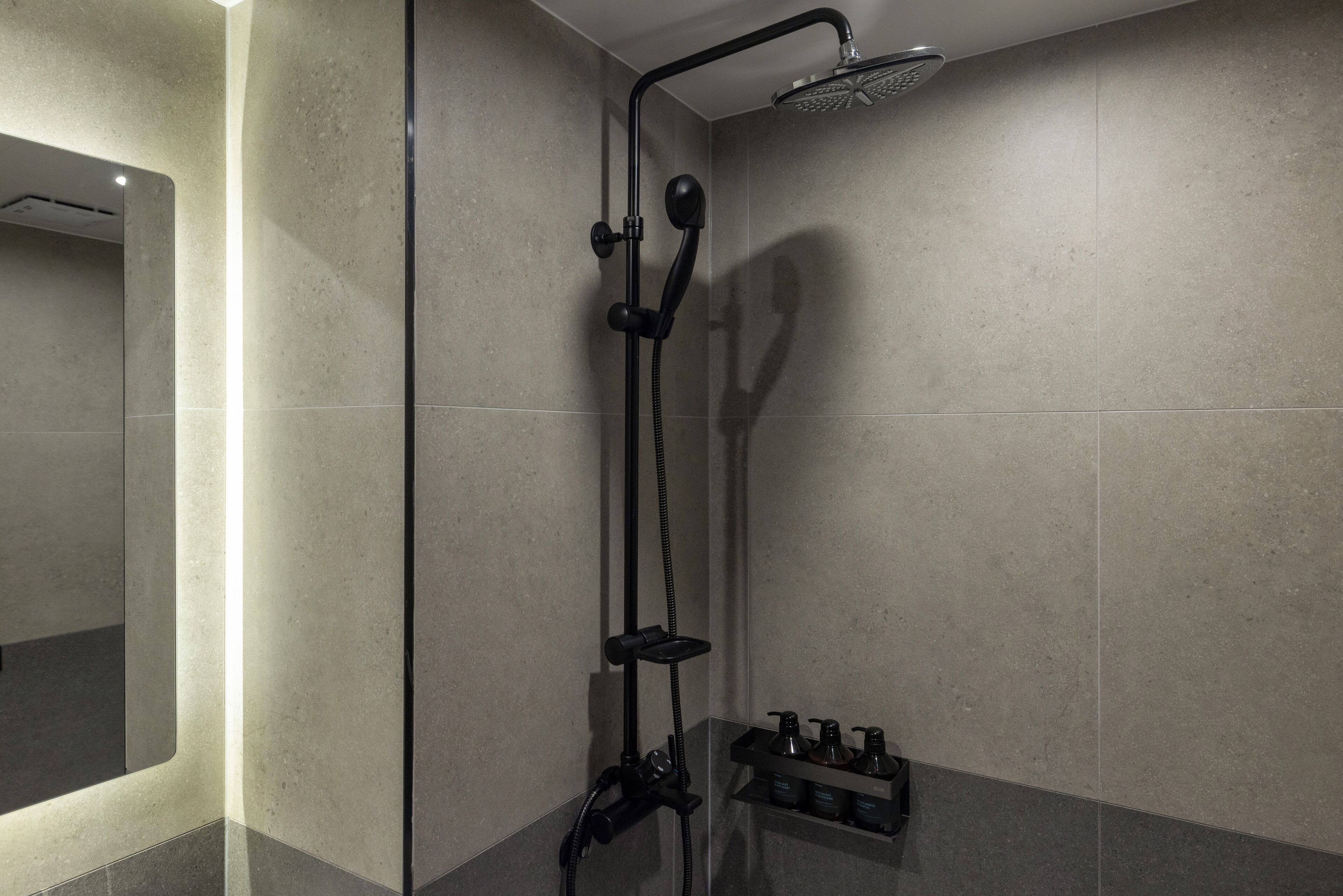 A modern bathroom with a shower, a mirror, and a shelf with toiletries.