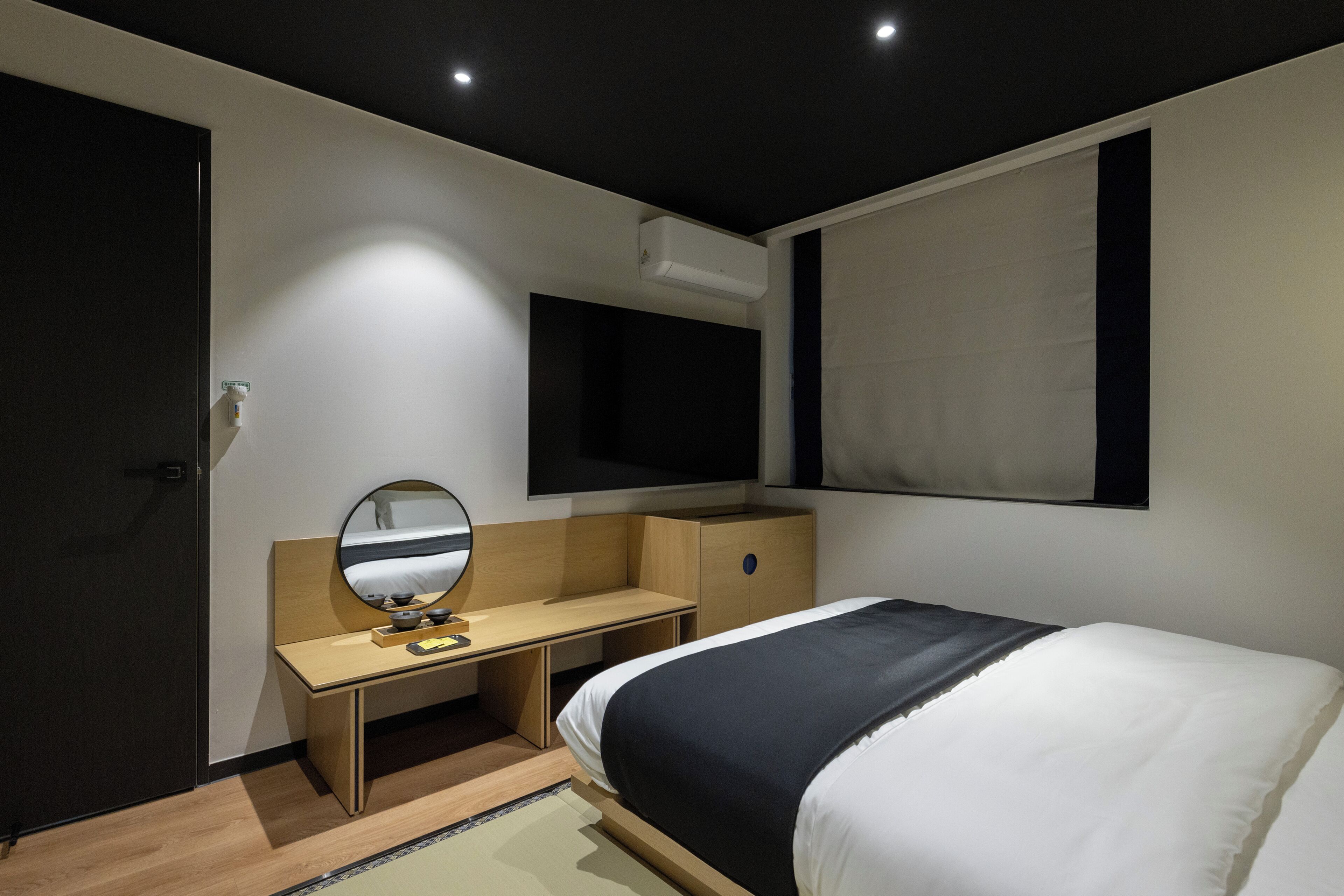 Una camera d'albergo moderna con un letto, una scrivania, uno specchio e una TV a parete.