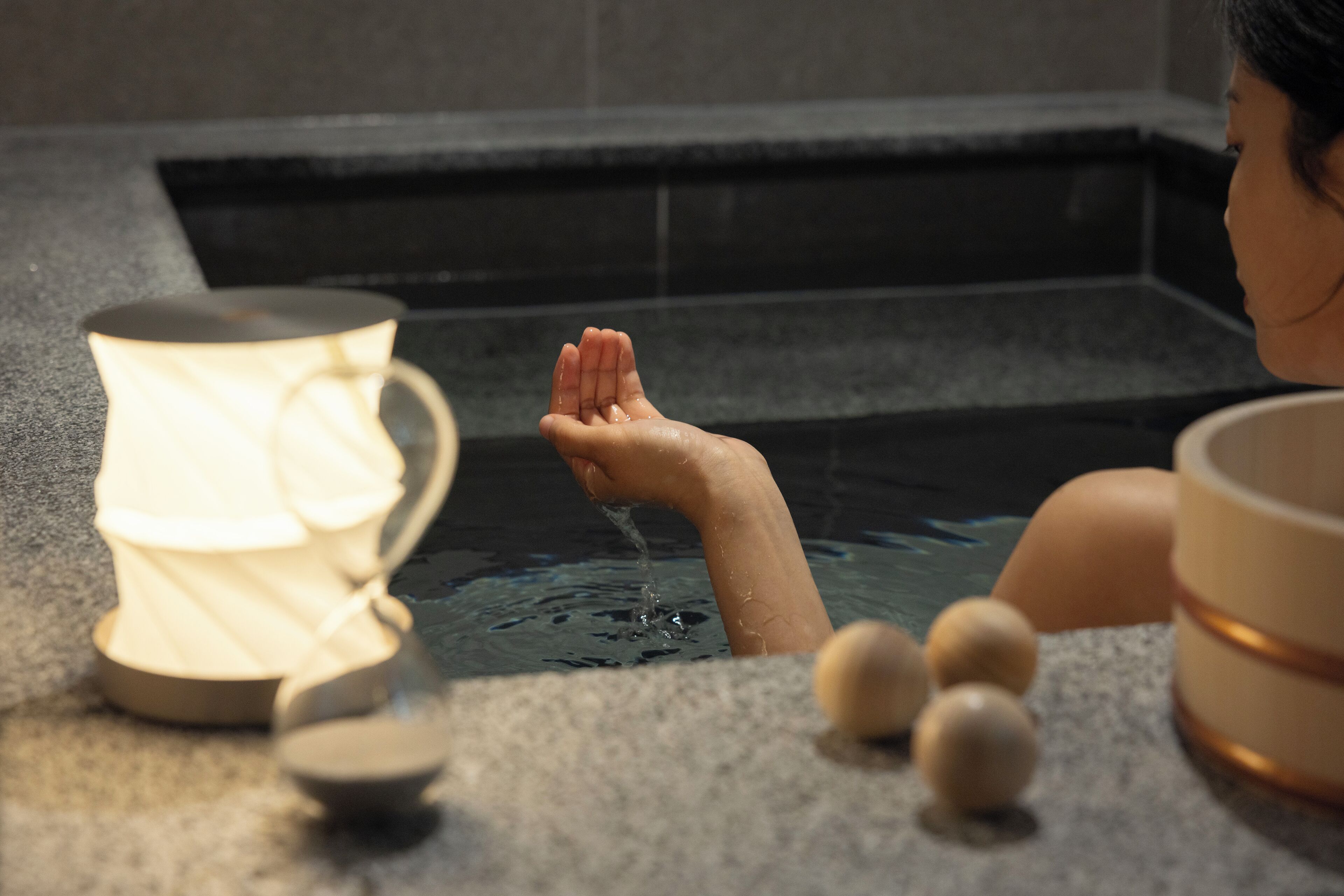 A person in a bathtub with a cup and wooden balls.