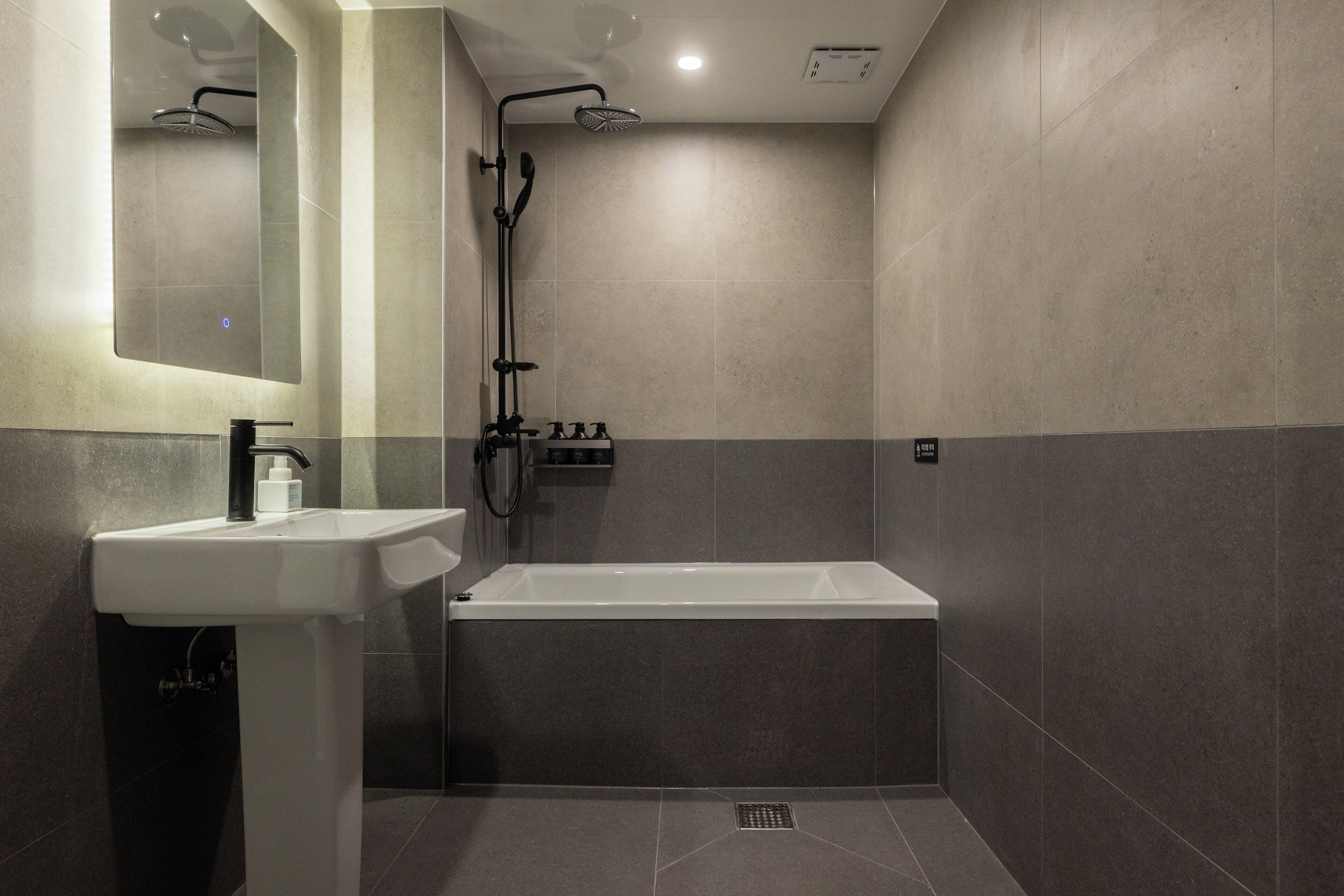 A modern bathroom with a white sink, a bathtub, and a showerhead.
