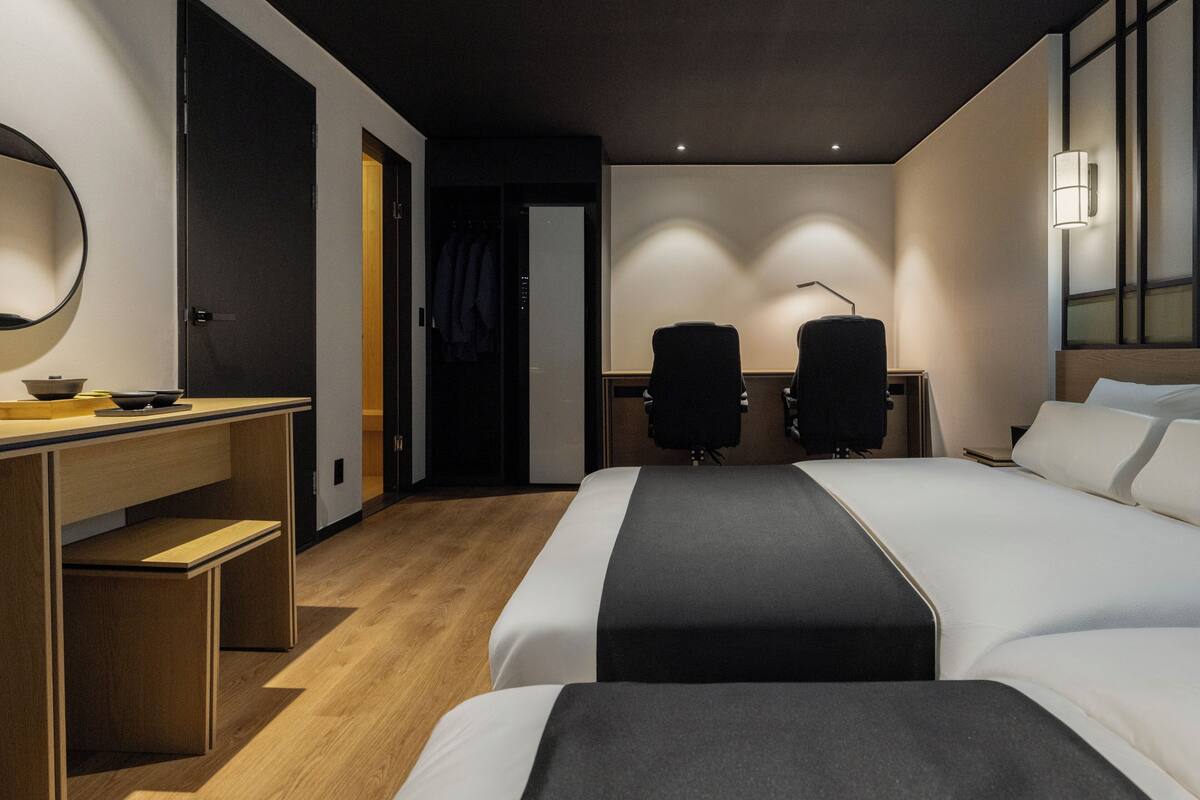 Quarto de hotel com cama, escrivaninha, duas cadeiras, espelho e abajur.