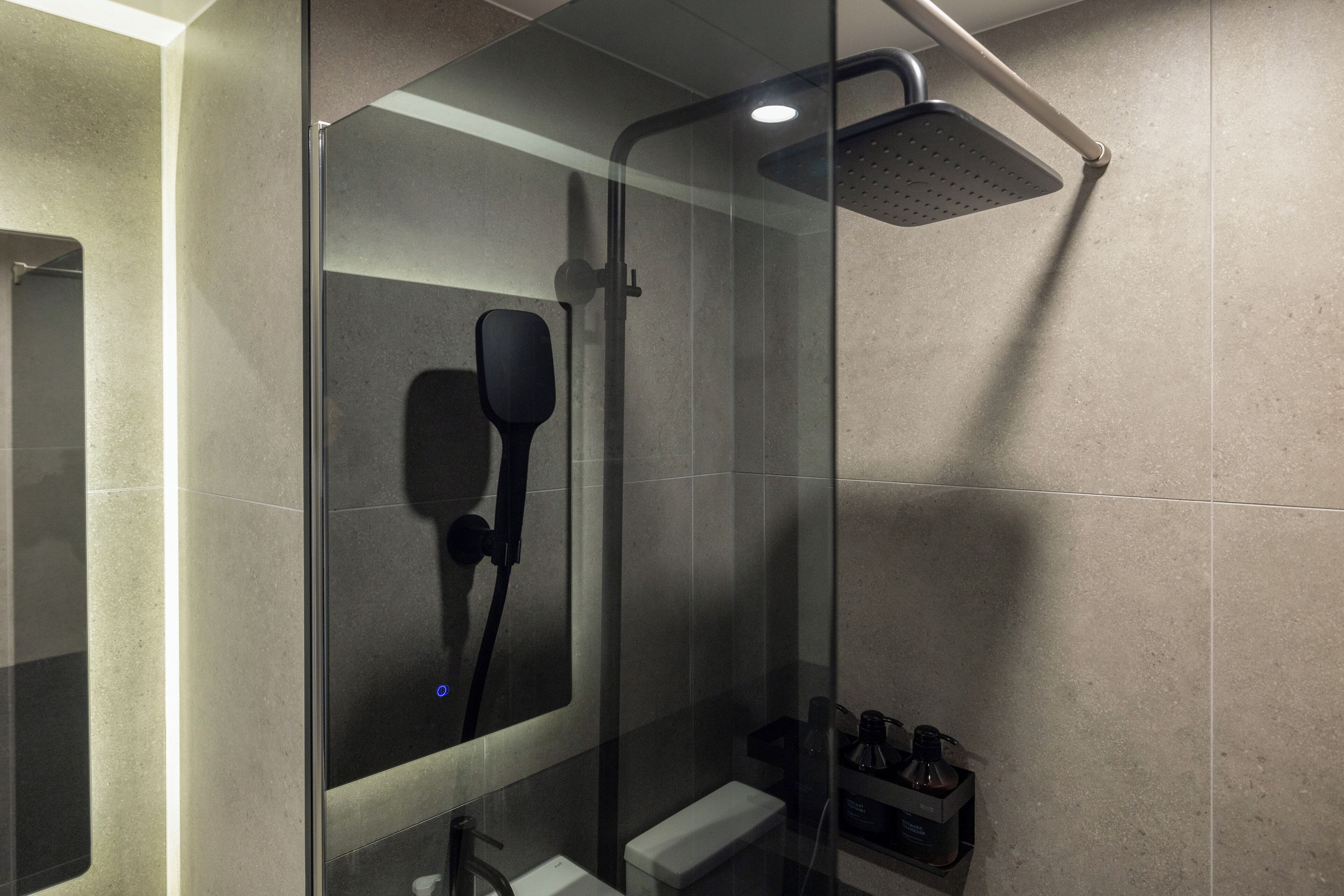 A modern shower with a glass enclosure, a handheld showerhead, and a small shelf with toiletries.