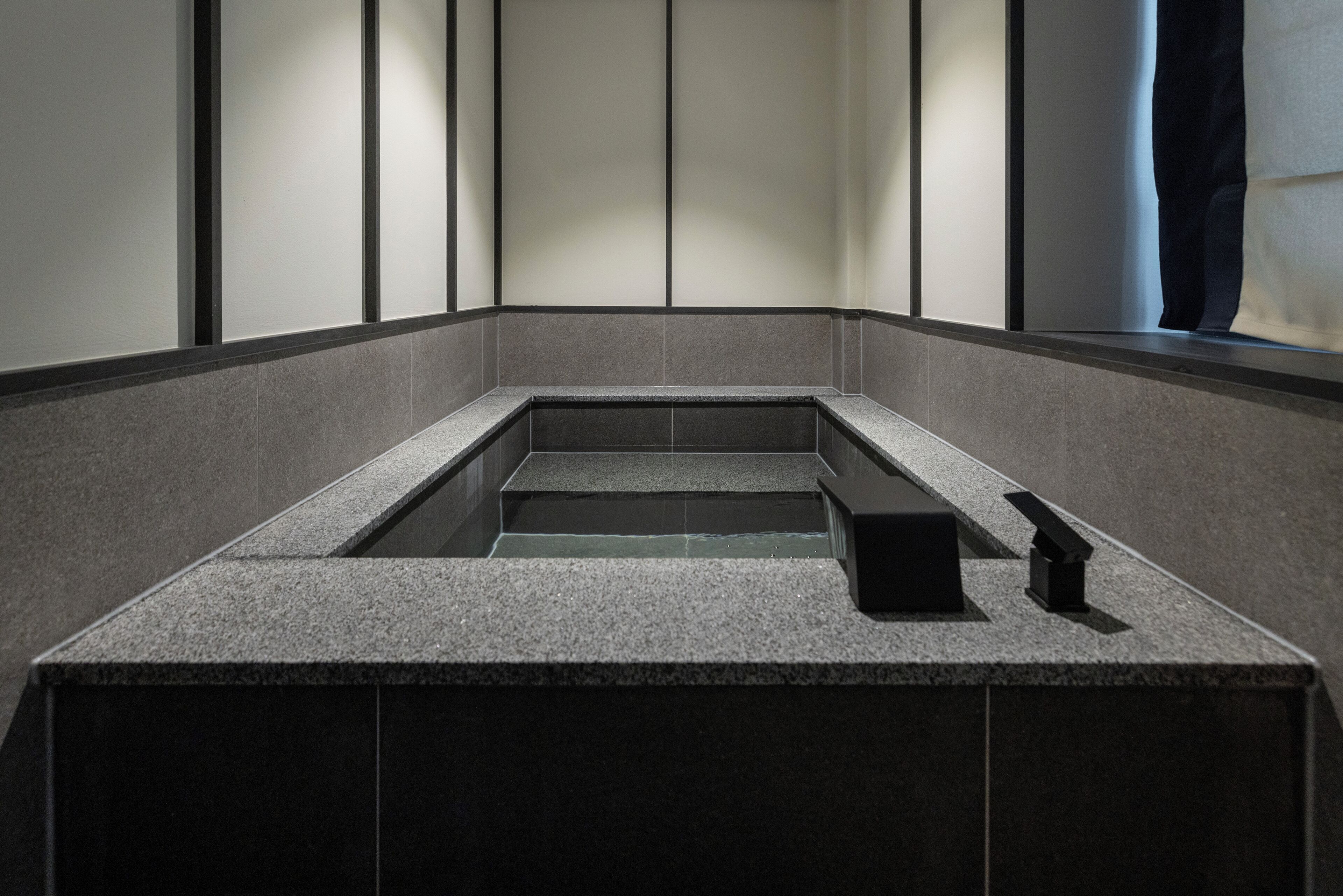 A modern bathroom with a rectangular sink, dark tiled walls, and a window with a curtain.