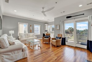 Una sala de estar amplia con ventilador de techo, una mesa de centro de vidrio y dos sofás.