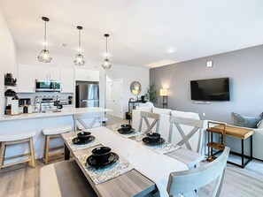 Una cocina moderna con armarios blancos, un refrigerador de acero inoxidable y un comedor con una mesa blanca dispuesta para cuatro comensales.